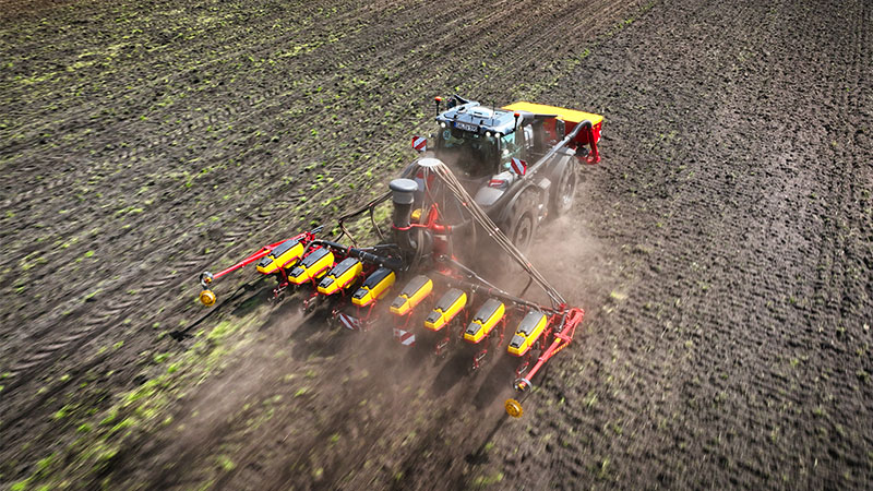 Valtra tractor operating a multi-row precision seed drill across a cultivated agricultural field. Dust is visible behind the implement as seeds are being planted into prepared soil, highlighting active field work during the planting season. The combination of tractor power and precision seeding technology supports efficient crop establishment and consistent field coverage. The aerial perspective emphasizes large-scale arable farming operations and the role of advanced agricultural machinery in modern crop production. The asset reflects Valtra's connection to productive field performance and professional farming applications.