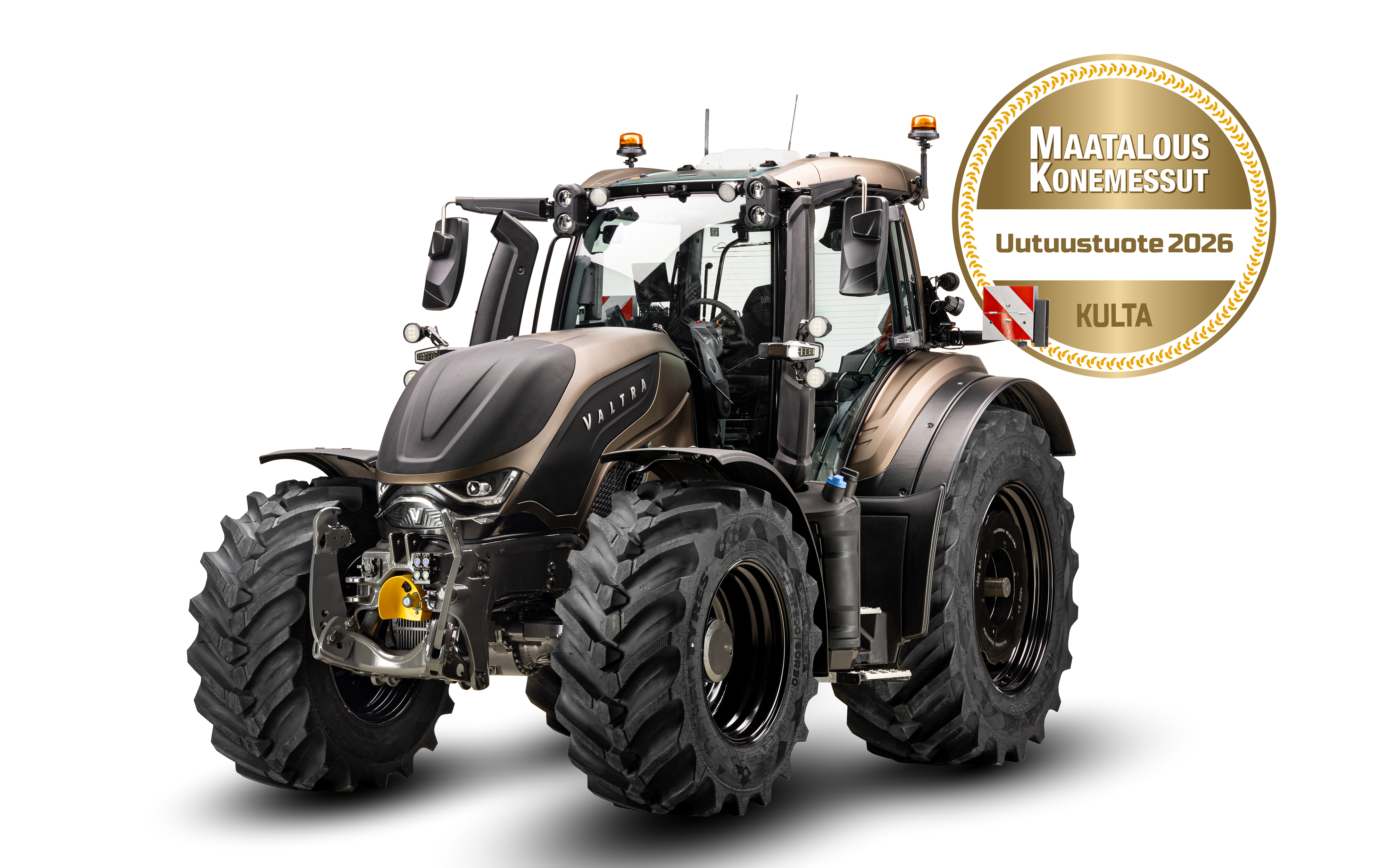 A Valtra T Series agricultural tractor is shown isolated on a white background. The cab features visible lights, mirrors, and safety equipment, emphasizing advanced farm machinery design. To the right, a circular gold badge reads "MAATALOUS KONEMESSUT" and "Uutuustuote 2026" with a red and white ribbon and the word "KULTA," indicating a 2026 new product gold recognition. The overall image focuses on professional farming equipment and its award-winning status.
